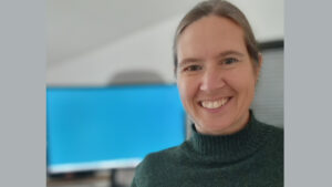 Porträtfoto Henriette Schwarzer mit PC-Monitor im Hintergrund.